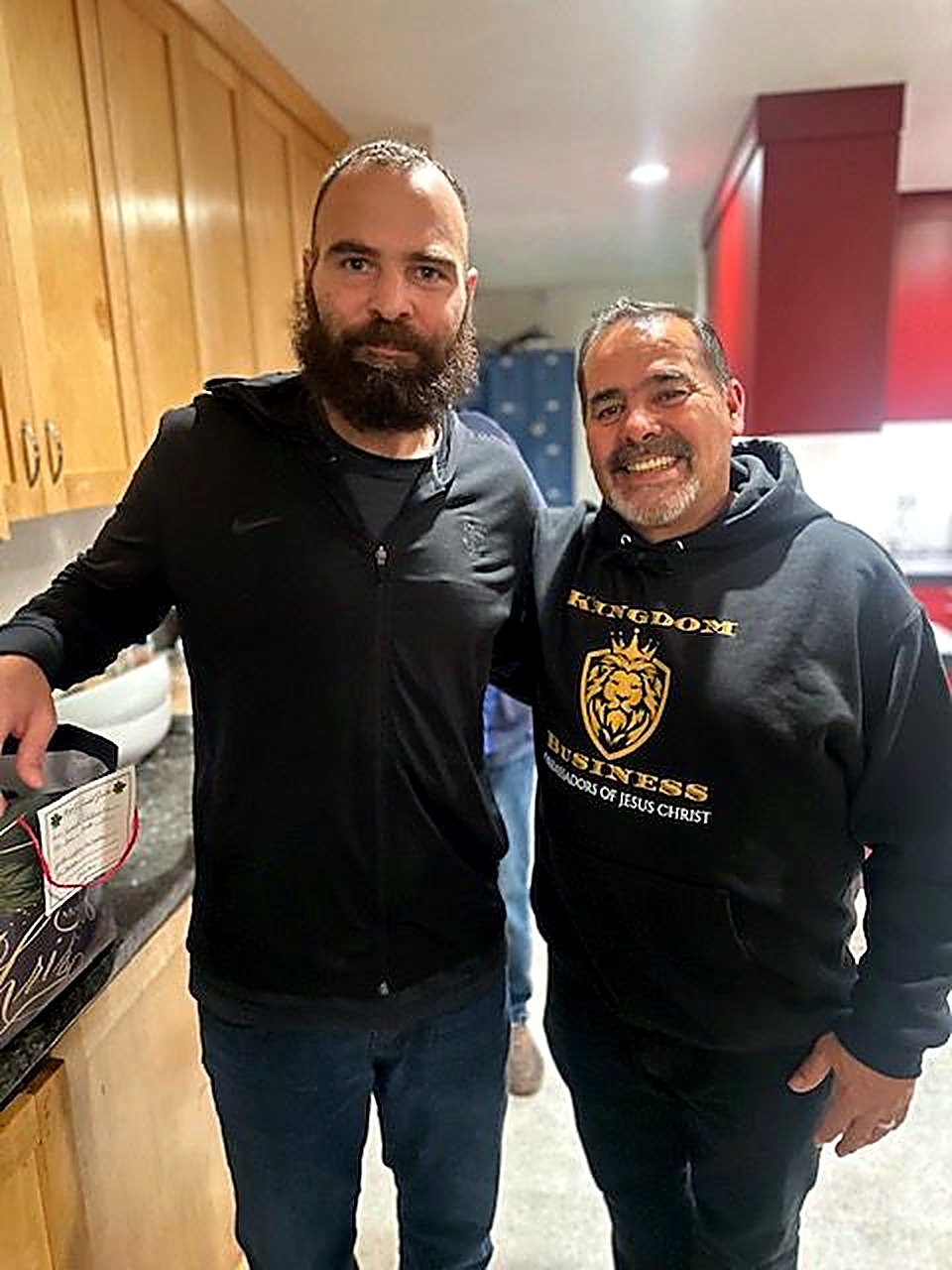 Two men standing together, one wearing a faith-based hoodie